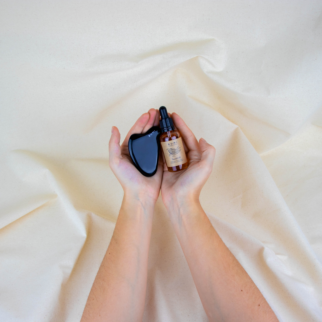 gua sha lifestyle image with face oil in palm of hand with white fabric background