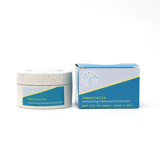 image of coraline skincare' immortelle everlasting radiance facial balm on a white background, the product comes in a sulapak bioplastic jar which is white with orangey colours flecks on it. The label and the box is a light blue triangle, a yellow diviidng line and a sea blue triangle