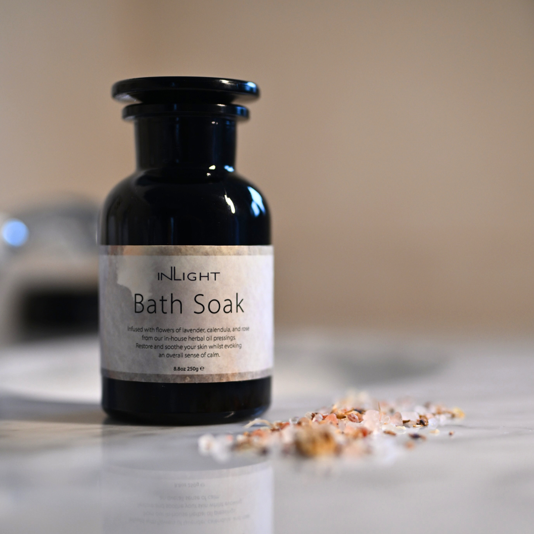 Bottle of 'INLIGHT Bath Soak' on a neutral background with salts and dried florals sprinkled in the foreground
