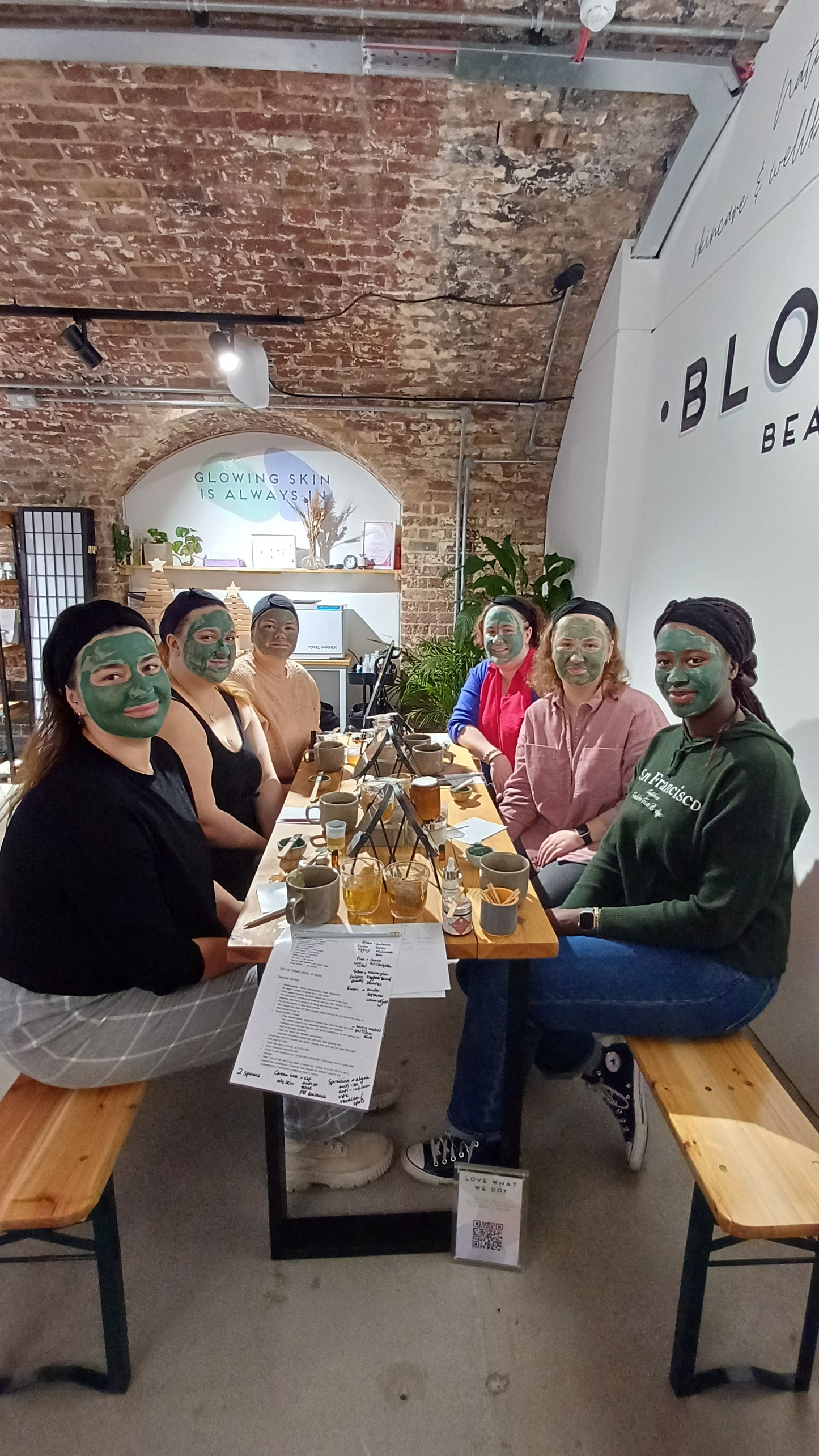 group photo of attendees of our clay face mask class in london. they have made their own face masks and have blended them to apply on their skin in the class. they are sitting enjoying the face mask on their face before cleansing it off.