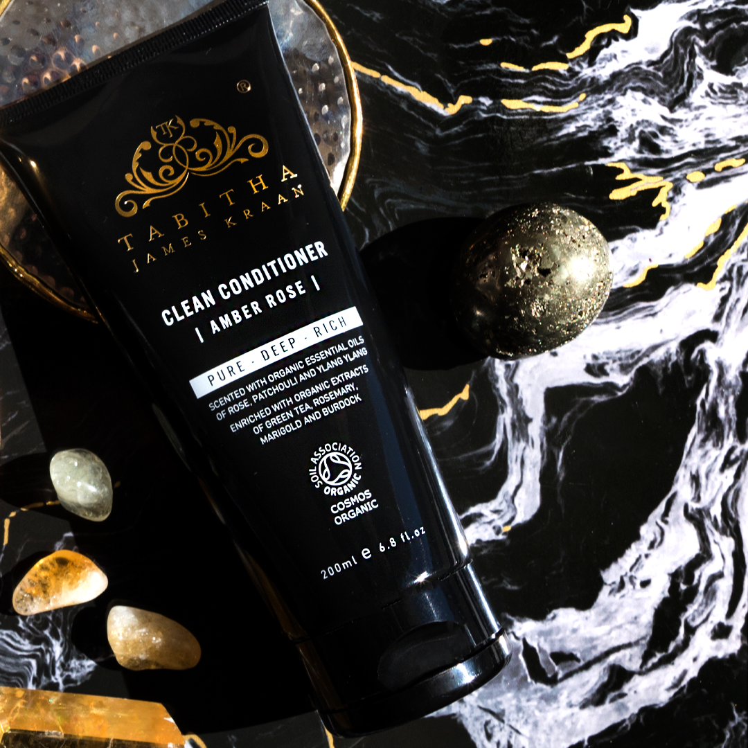 black bottle of organic hair condition on dark black and gold marbled surface with crystals dotted around it