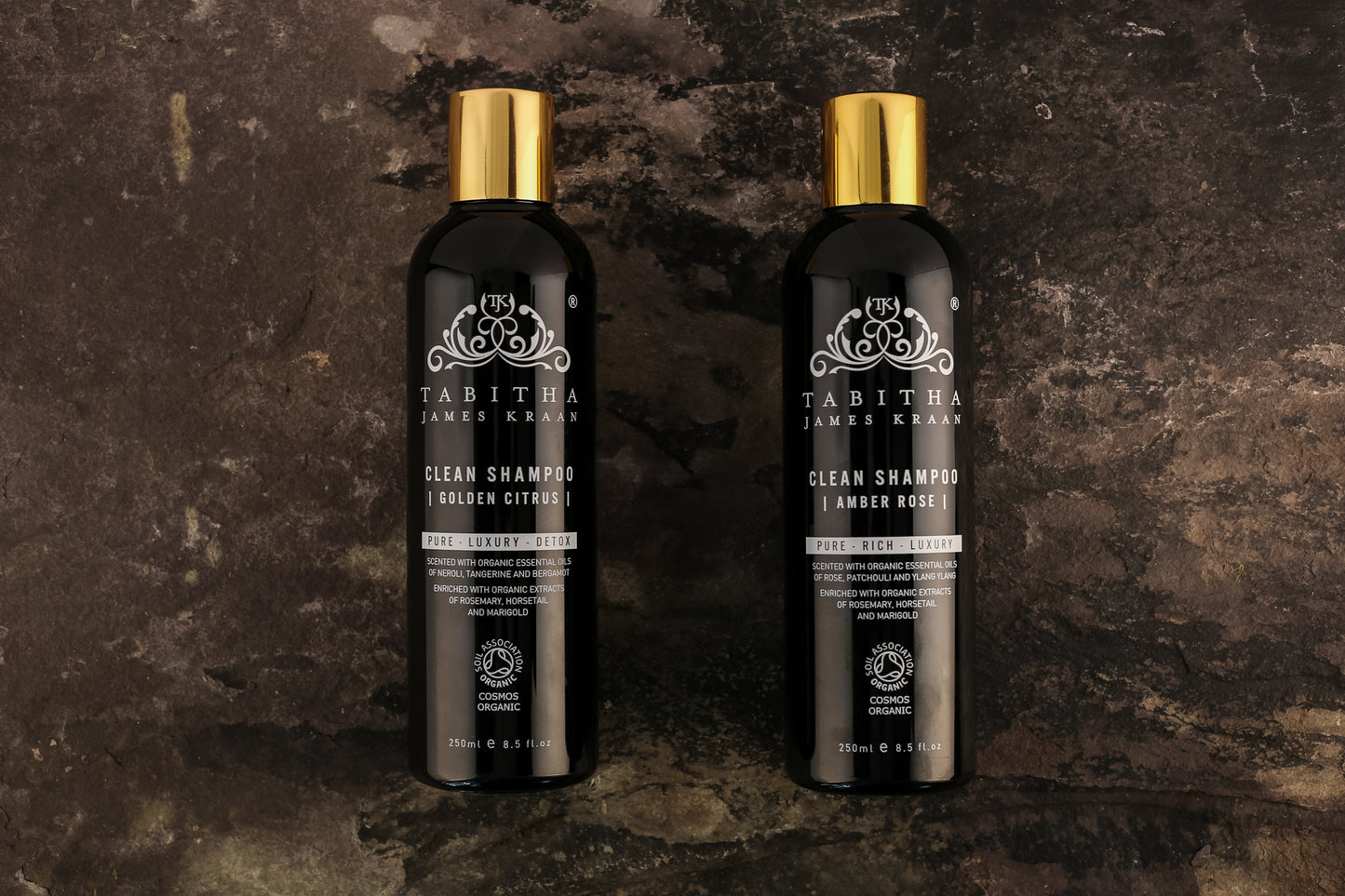 tabitha james kraan clean organic shampoo in golden citrus and amber rose scents laid side by side on a dark brown grey marble background