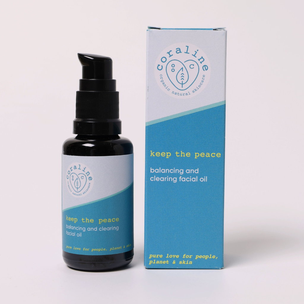 photo of the coraline skincare keep the peace face oil which is for oily, combination and break out prone skin. White background image with the face oil black glass bottle visible on the left of the image. the bottle has a black pump and a light blue and turquoise blue label. to the right side of the image is the outer box packaging. the label reads 'coraline organic natural skincare. keep the peace balancing and clearing facial oil. pure love for people, planet and skin