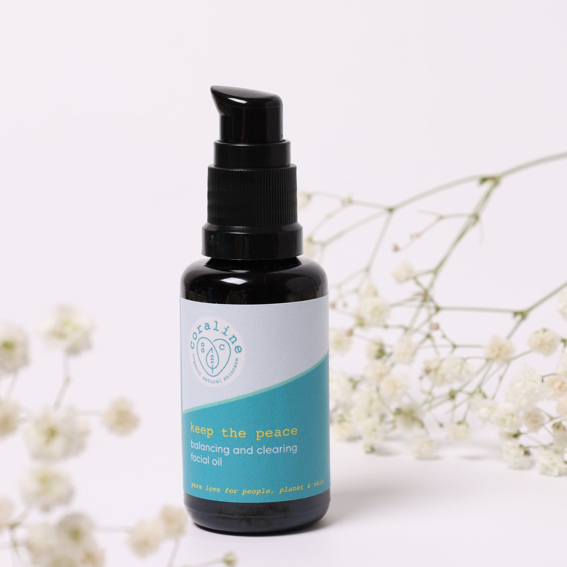 full sized coraline keep the peace face oil which is pictured in its black glass bottle with black plastic pump lid and a light sky blue and turquoise logo with yellow and white text. the face oil which is for oily and combination skin to help clear up spots, acne and pimples is pictured on an off white background with gypsohila flower fronds slightly blurred in the background
