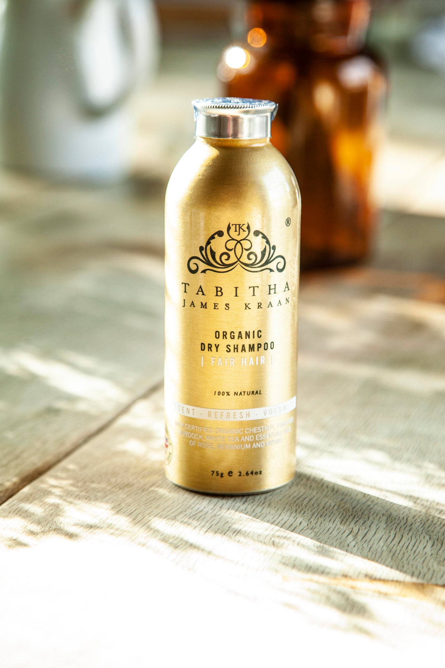 shot of the gold aluminium dry shampoo shaker bottle bathed in soft sunlight with blurred vases in the background
