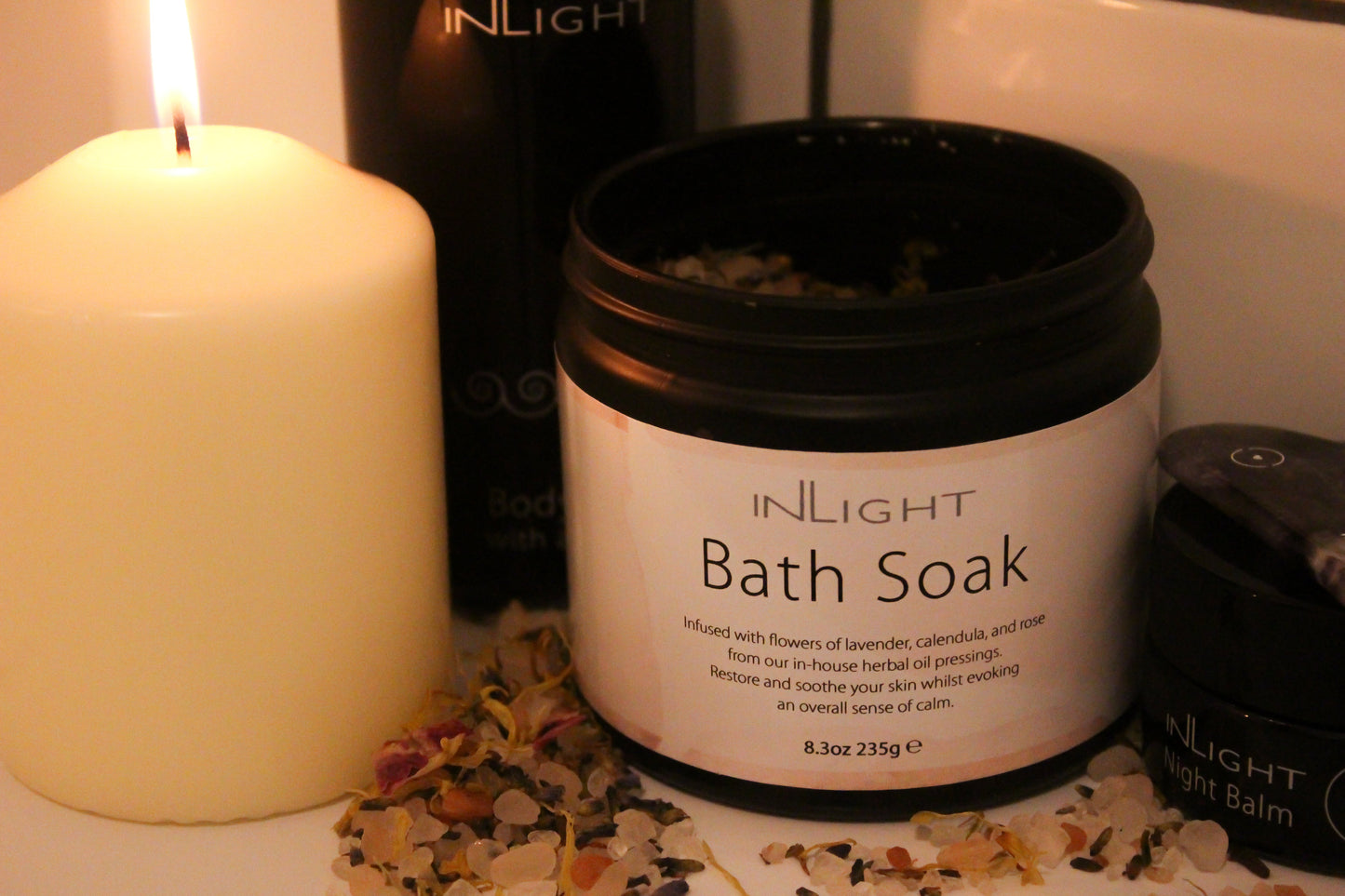 cosy scene with inlight beauty bath salt jar sitting amongst other inlight organic skincare products and a white creamy candle surrounded by the bath salts scattered