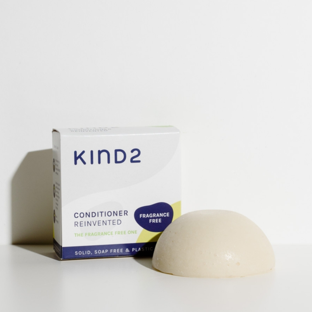 Dome shaped off-white plastic free KIND2 conditioner bar. Placed next to the grey and white box it comes in.