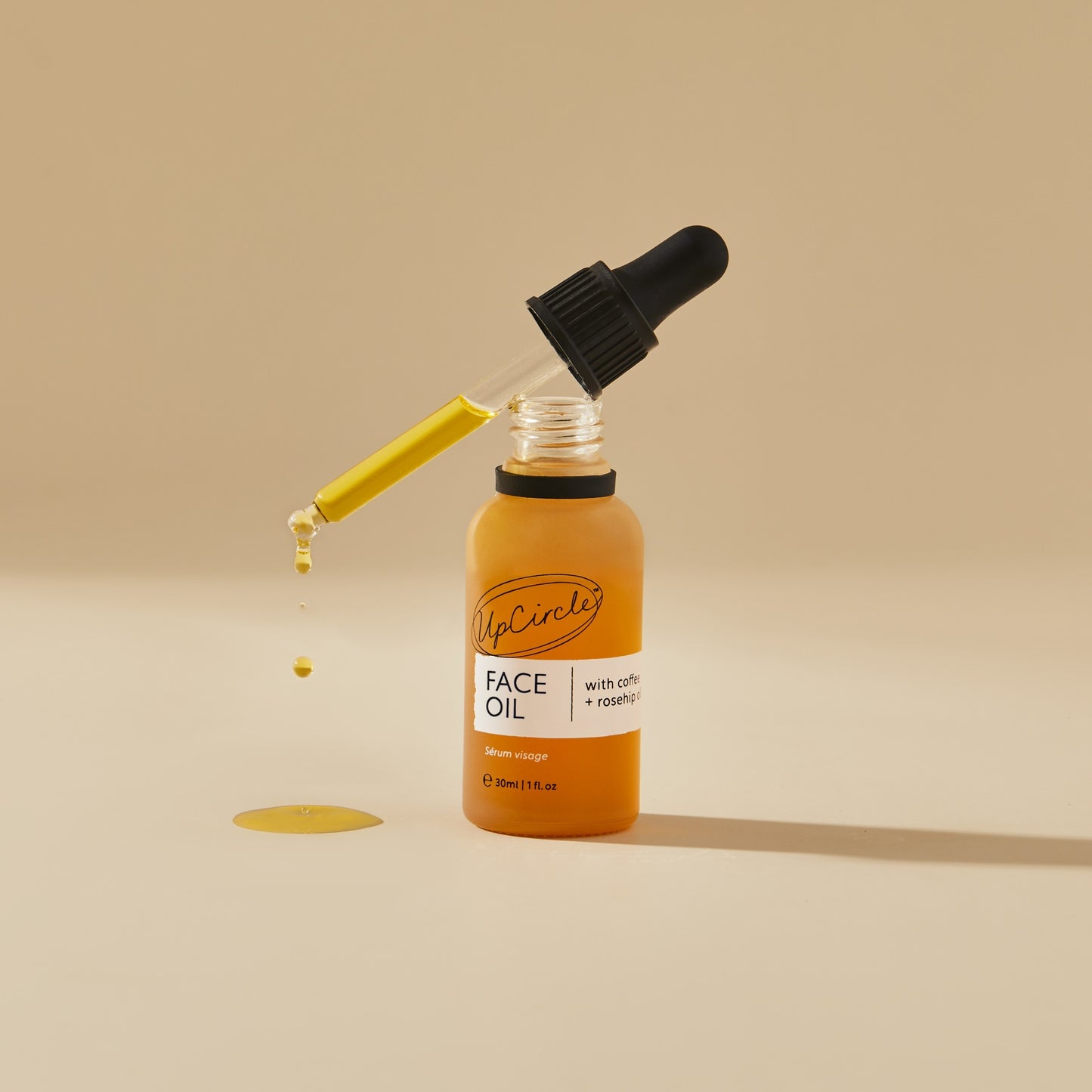 photo of upcircle's facial oil bottle with the glass pipette sitting on top of it, dripping the golden coloured oil on to a creamy background