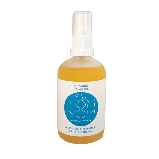 photo of nom nom's organic relax oil, a multipurpose natural oil blend for face and body. The bottle of oil is on a white background. the bottle is a slightly frosted bottle but you can still see the yellow coloured botanical oils inside it. the bottle has a plastic pump lid and a white label with blue accents. the label reads ' organic relax oil. nom nom without within, lavender chamomile and frankincense'