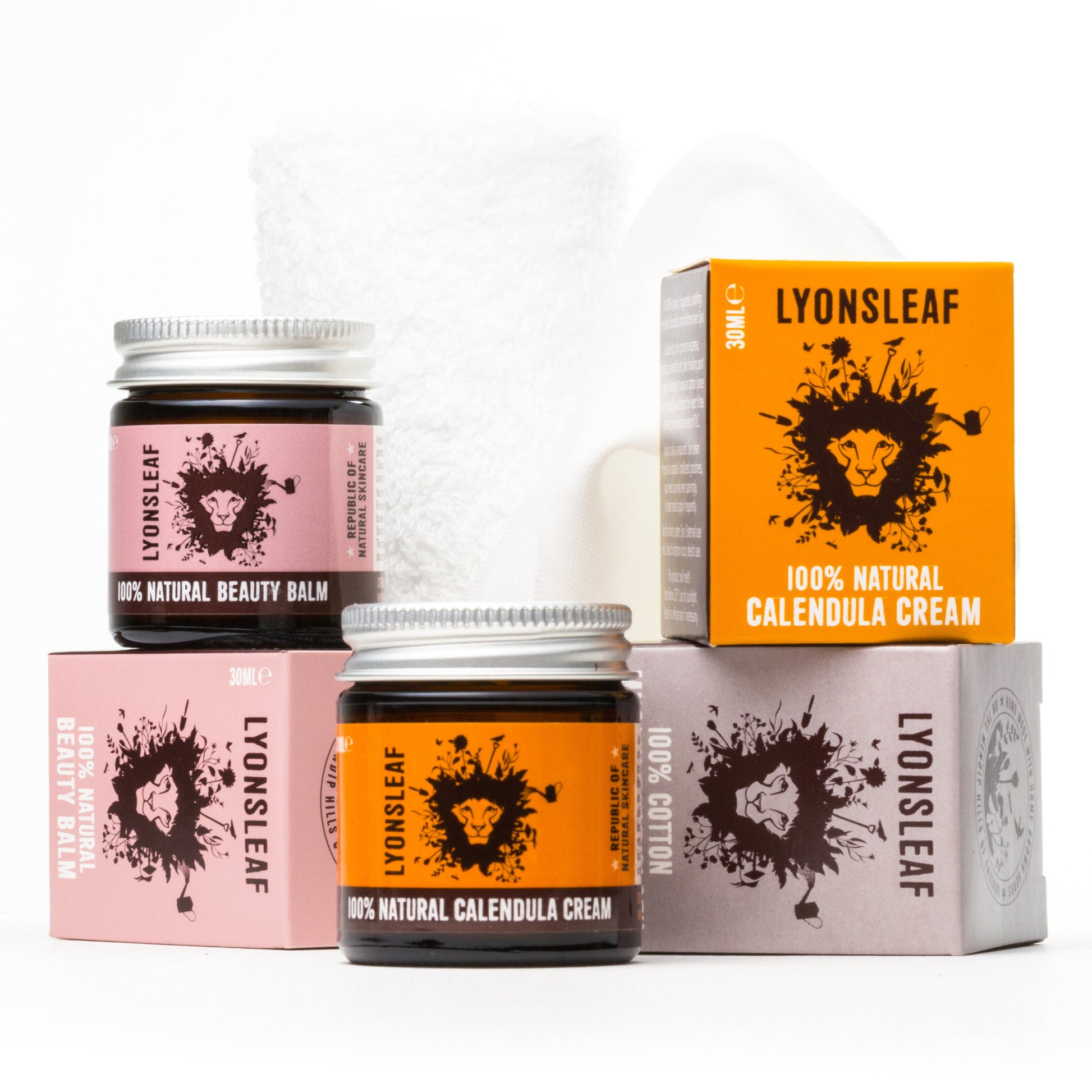 The image displays two jars and three boxes of Lyonsleaf skincare products. The jars are labeled "100% Natural Beauty Balm" and "100% Natural Calendula Cream." The boxes are similarly labeled and feature a lion's face design. A white cloth is also partially visible.