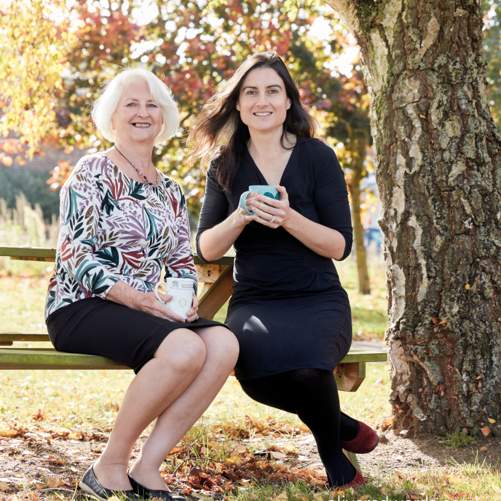 Image of Odylique founders, Margaret Weeds and her daughter Abi, sitting outside on a bench next to tree.