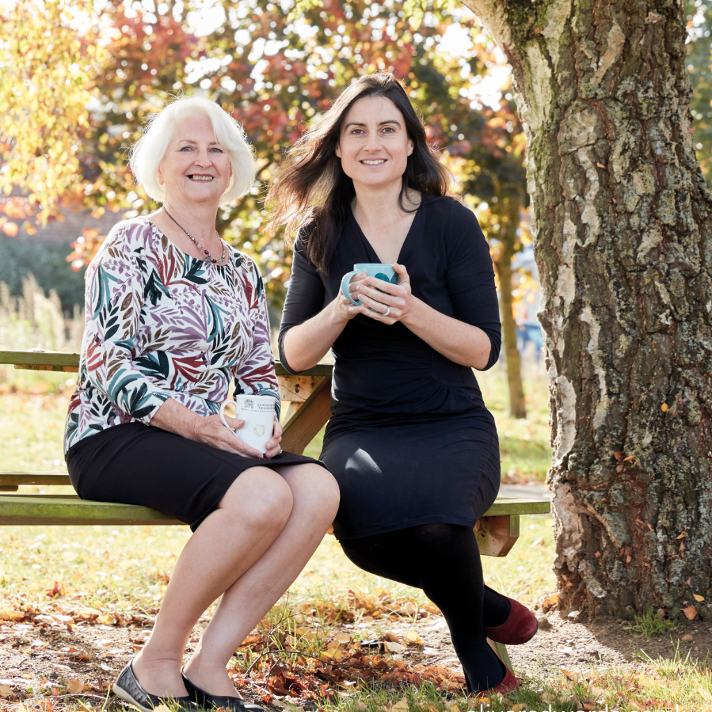 Image of Odylique founders, Margaret Weeds and her daughter Abi, sitting outside on a bench next to tree. 