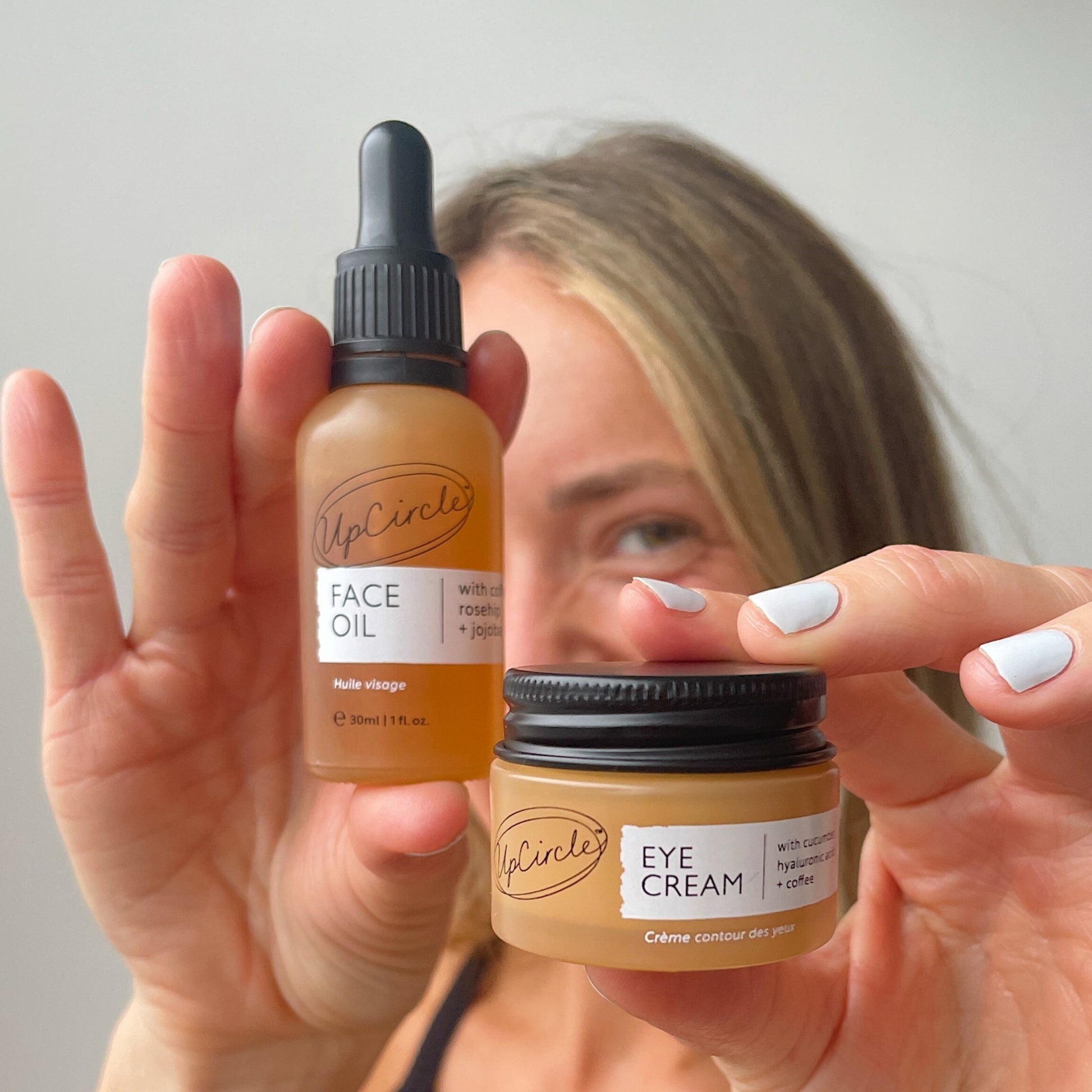 white woman with blondish hair holding up the upcircle face oil and eye cream which is part of the caffeinated duo set