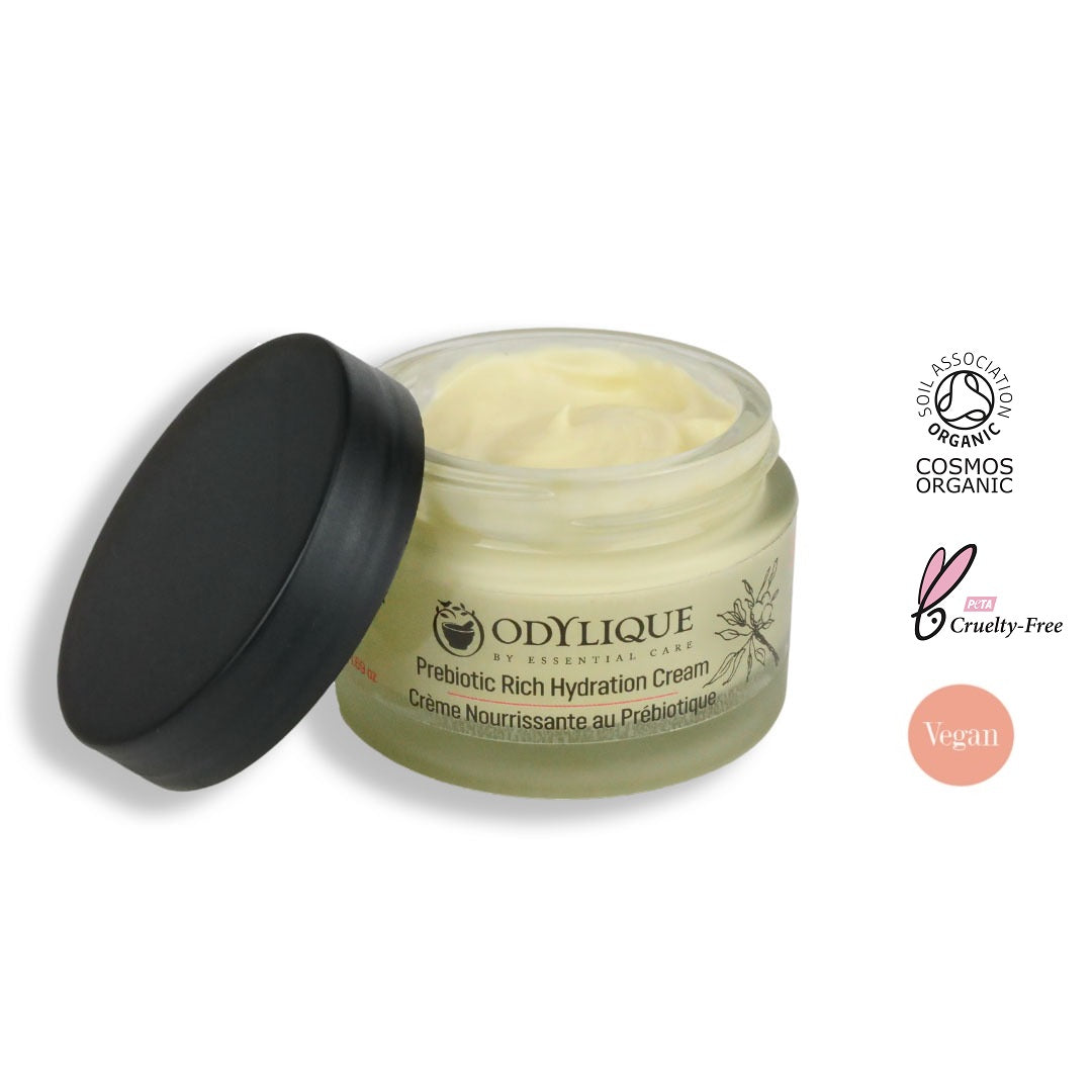An image of the “Odylique Prebiotic Rich Hydration Cream” against a white. The glass jar partially open with the lid resting against it. The soil association, cruelty-free and vegan certified logos displayed next to the image.