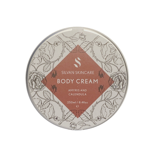aluminium tin filled with a creamy body moisturiser inside. the label on the tin features etches of the natural ingredients within the body cream and a dusky red diamond shape which has white text stating the name of the product silvan skincare body cream with amyris and calendula