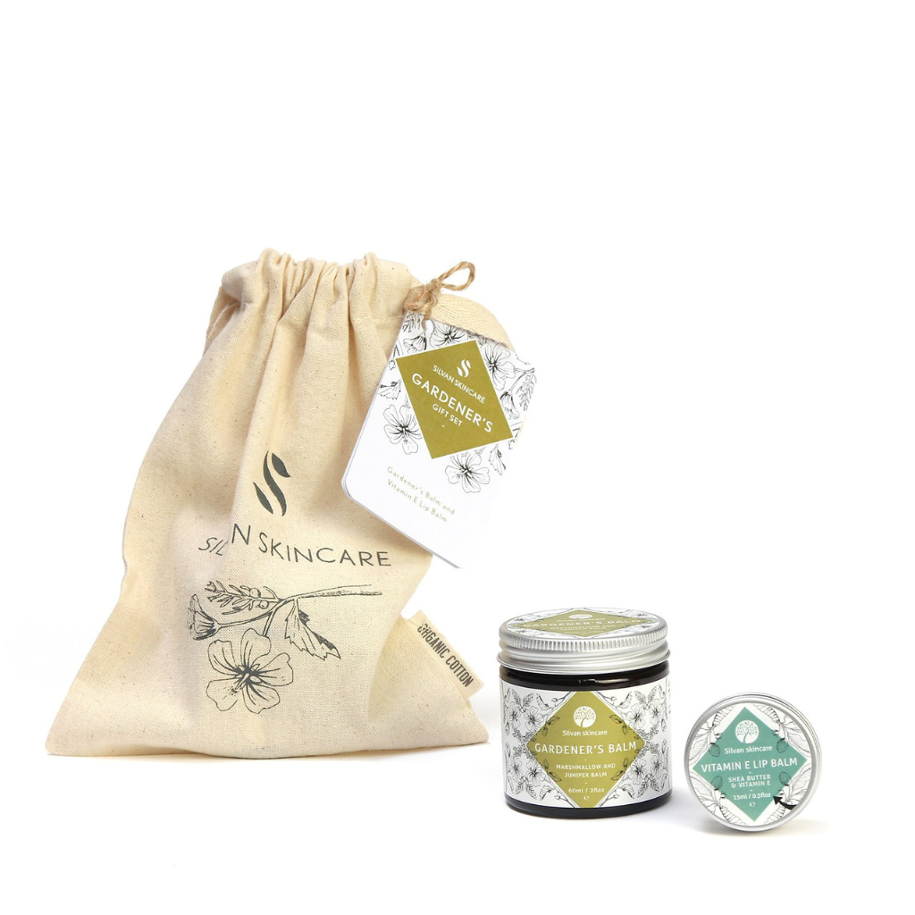 Silvan Skincare Gardener's Gift Set. Vegan gifts. The gift set is photographed on a white brackground. You can see the branded muslin cloth bag in the background with a white and green tag on it that reads ' gardener's gift set' in the foreground you can see the gardener's balm and vitamin e lip balm