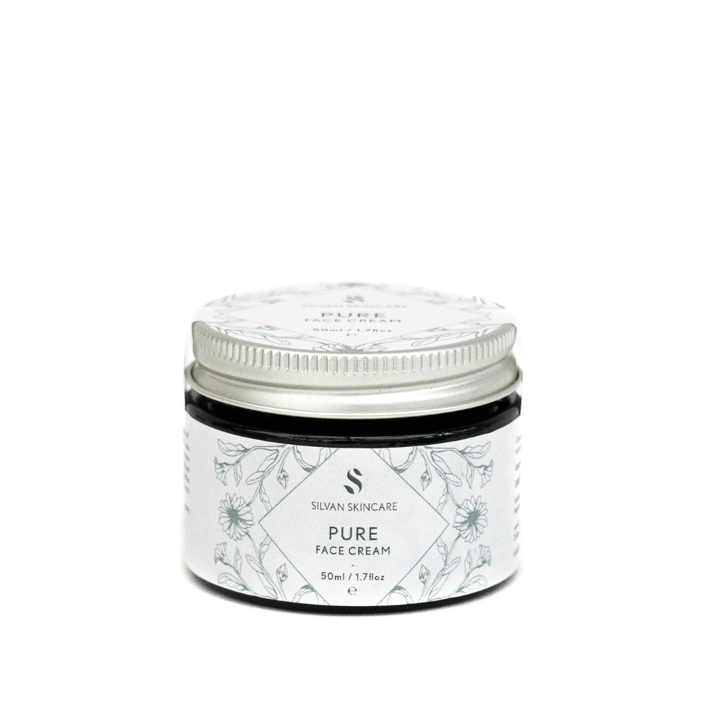 A glass jar of silvan skincare pure face cream. The small jar has an aluiminium lid and the labels are in white with blue botanical illustrations