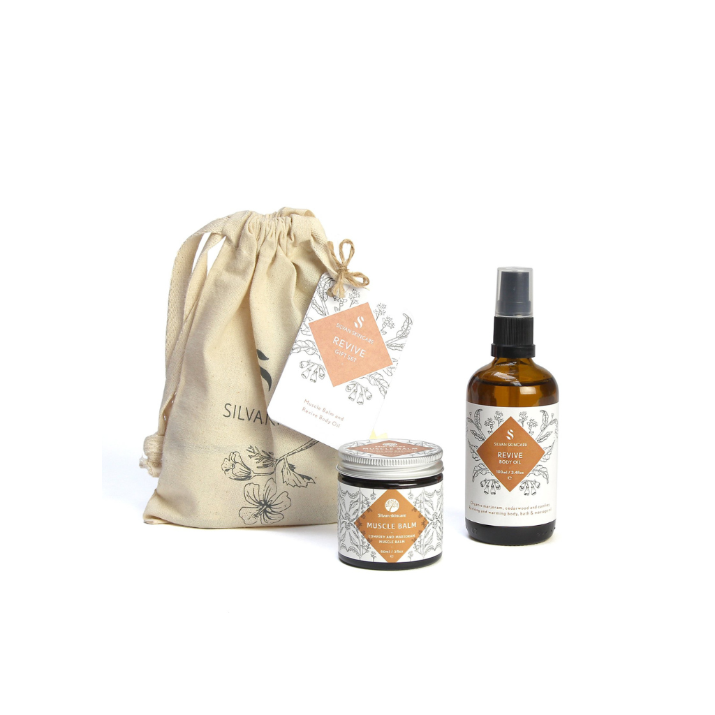 Silvan Skincare revive Gift Set. Vegan gifts. The gift set is photographed on a white background. You can see the branded muslin cloth bag in the background. In the foreground you can see the muscle balm and revive body oil.