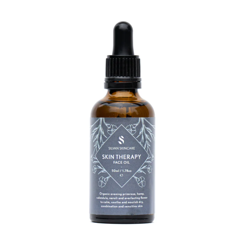 Silvan Skincare skin therapy face oil in an amber glass bottle with a dark blue label with white text listing the product and brand. The label also has light blue botanical illustrations.