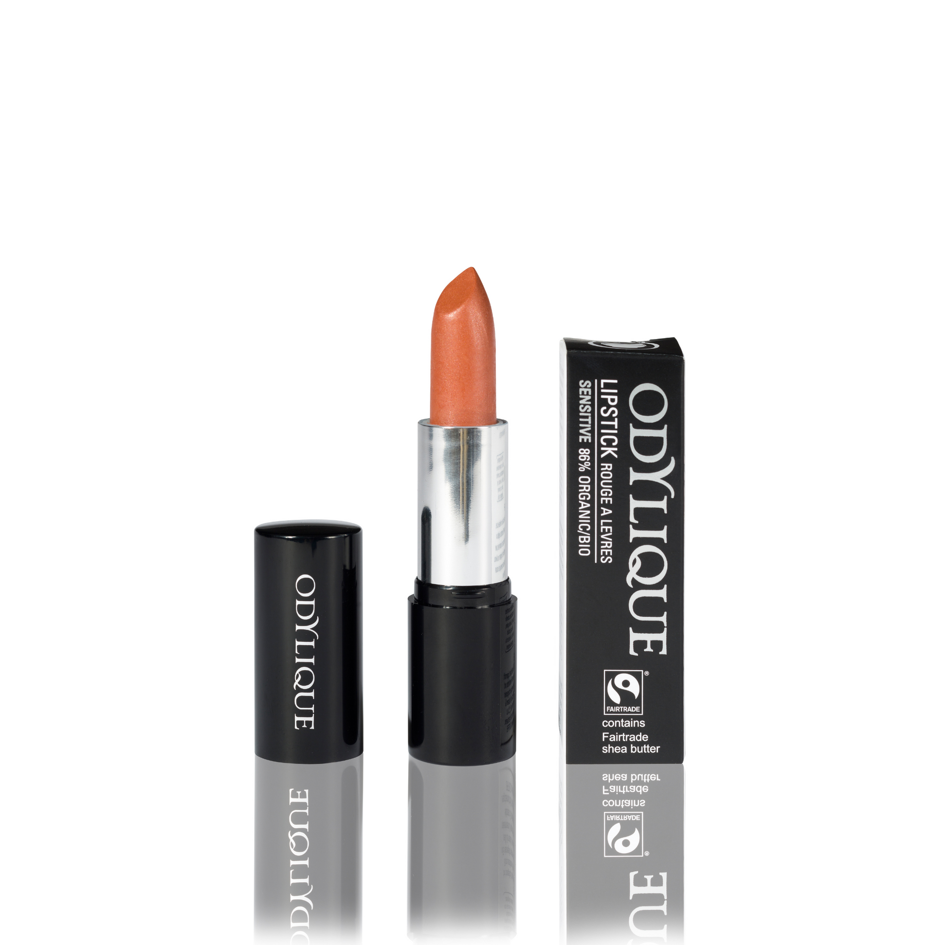 Odylique lipstick in apricot sorbet (orange) partially twisted up from its black tube, positioned next to its packaging on a reflective surface.