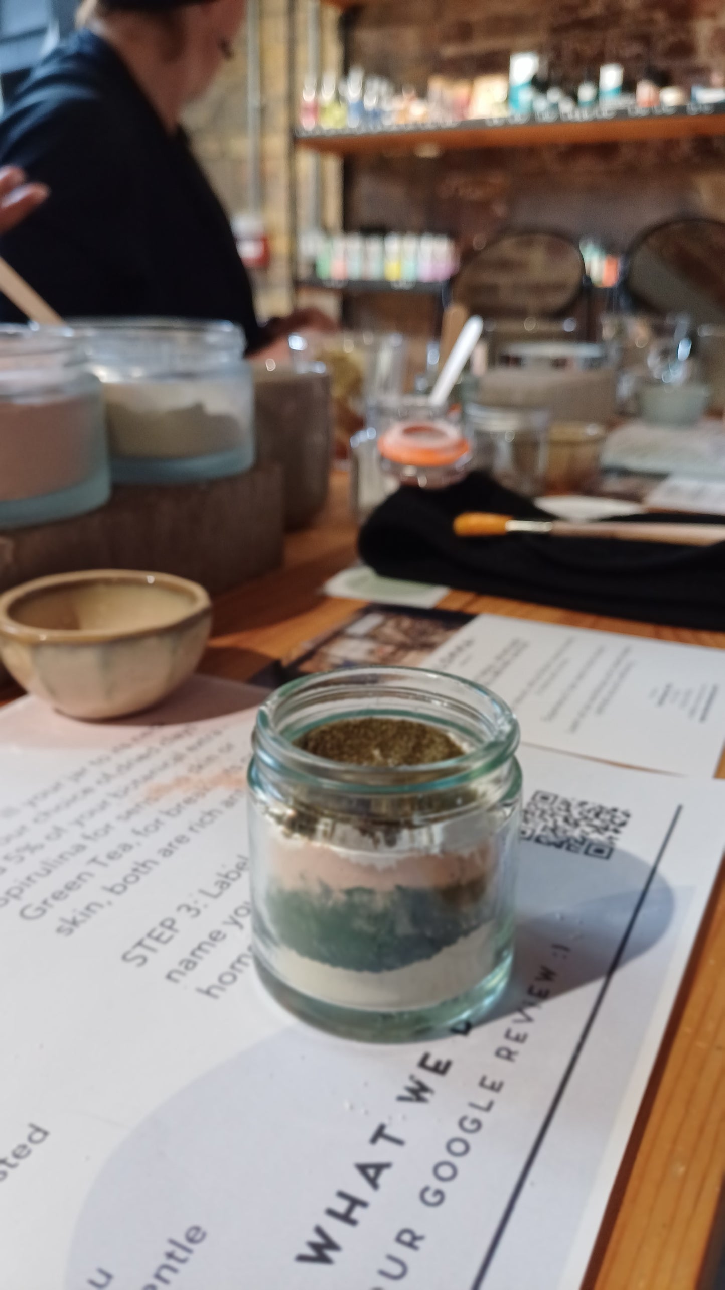 image of the clay face mask on the table in the middle of the class.showing the layers of the clay and skincare ingredients before they are blended together