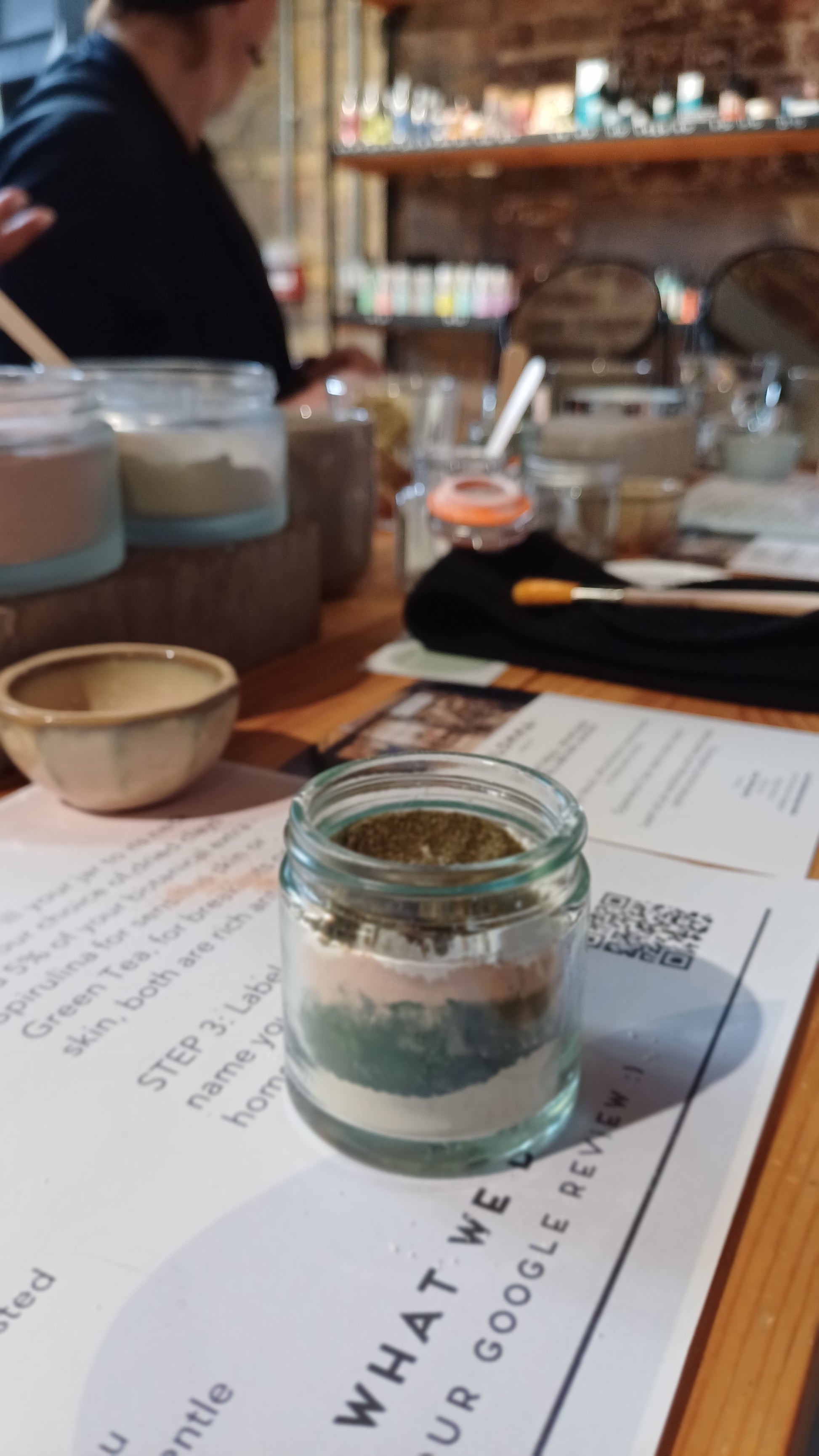 image of the clay face mask on the table in the middle of the class.showing the layers of the clay and skincare ingredients before they are blended together