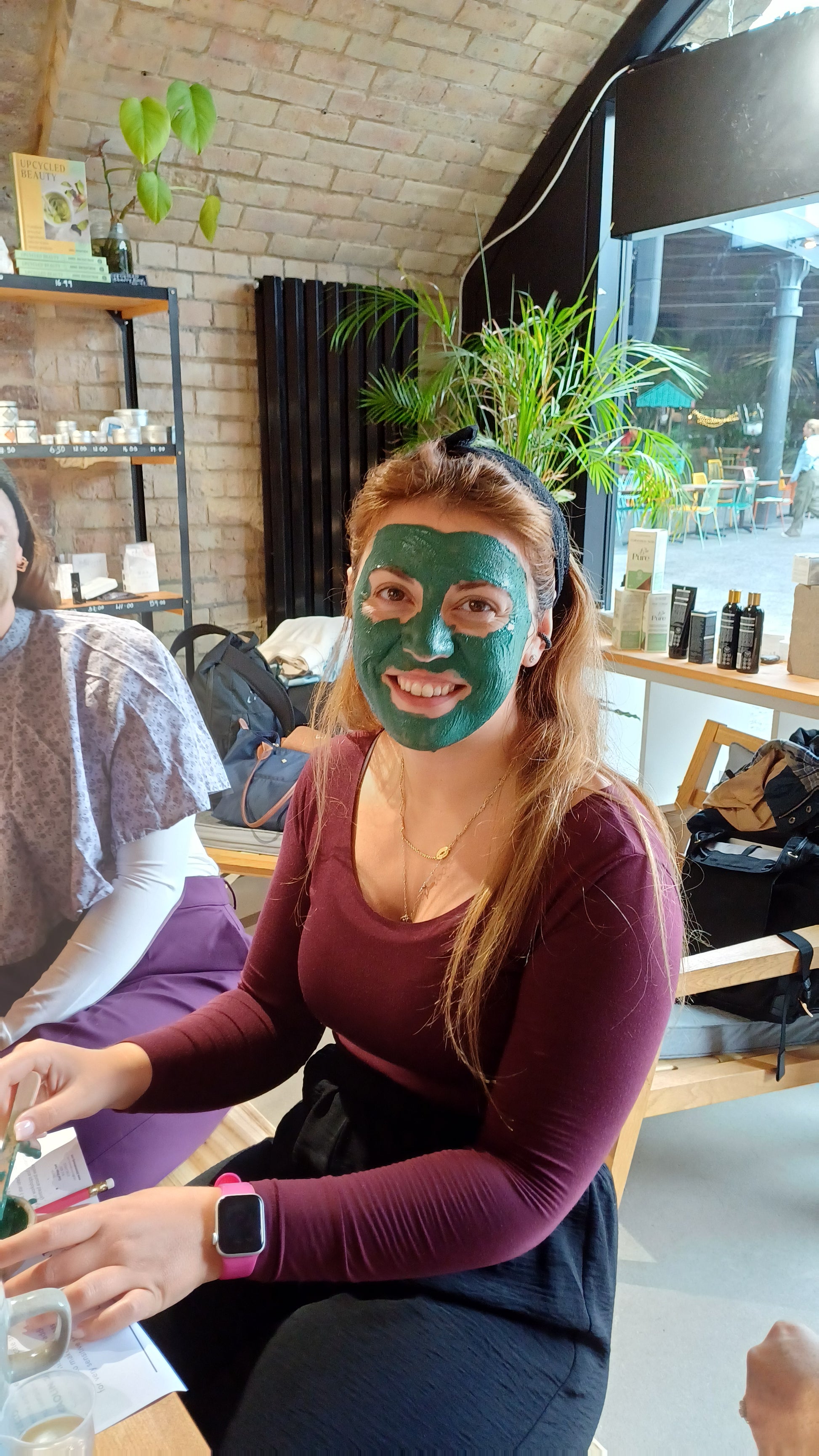 woman with red hair and a burgundy top with a green face mask on their skin