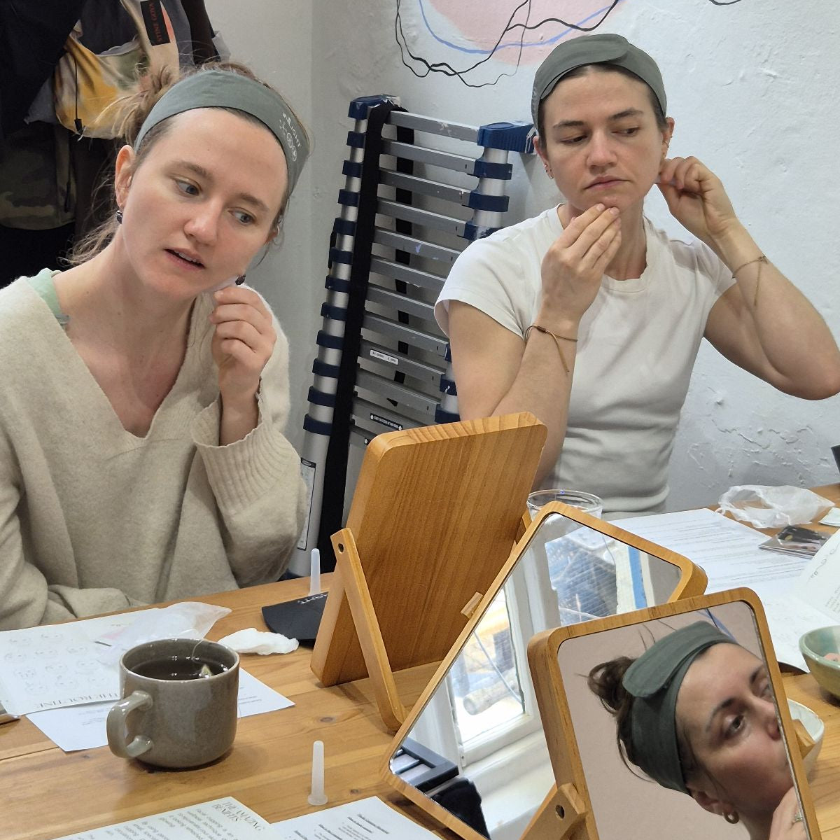 2 women wearing light coloured tops and headbands using facial cups
