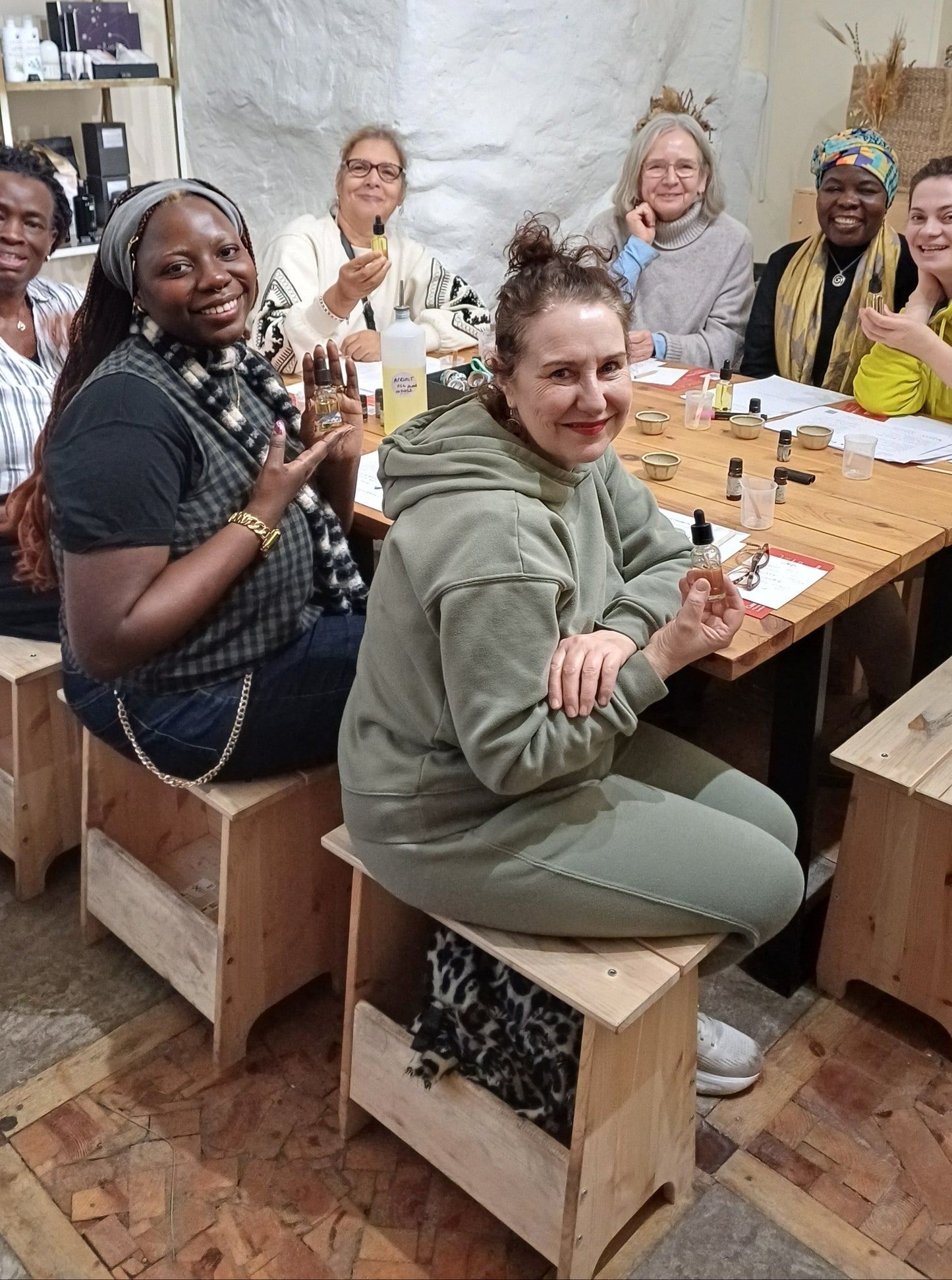 group of people sitting around a wooden table. they are making their own skincare oils infused with essential oils and crystals as part of a team celebration at work