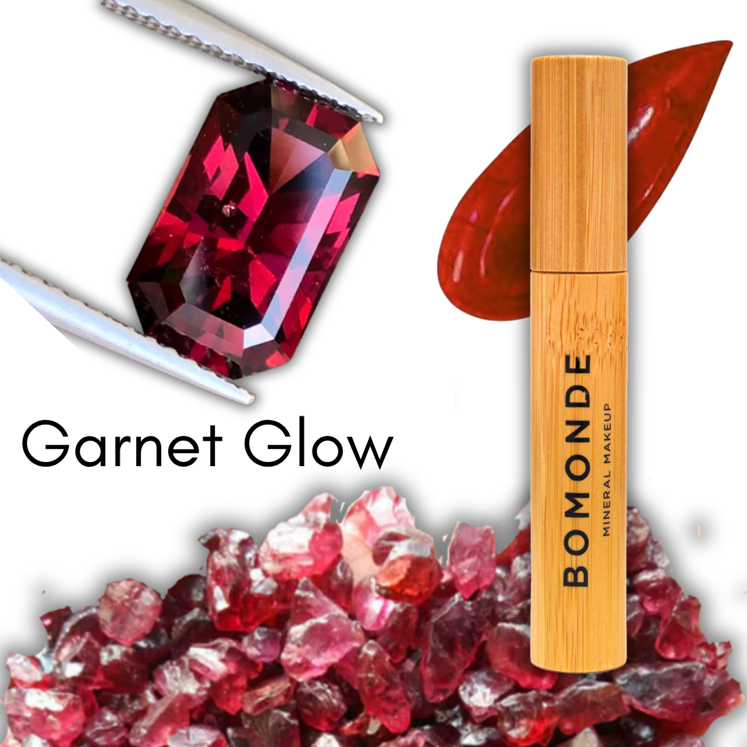 illustration to show the colour inspiration for vegan make up brand, bomonde's liquid lipstick, garnet glow, a deep shimmery red colour lip gloss. in the picture there is a clear red garnet gemstone held in tweezers and some shards of small garnet gemstone chips  next to the bamboo lipstick tube packaging and a swatch of the deep red gloss