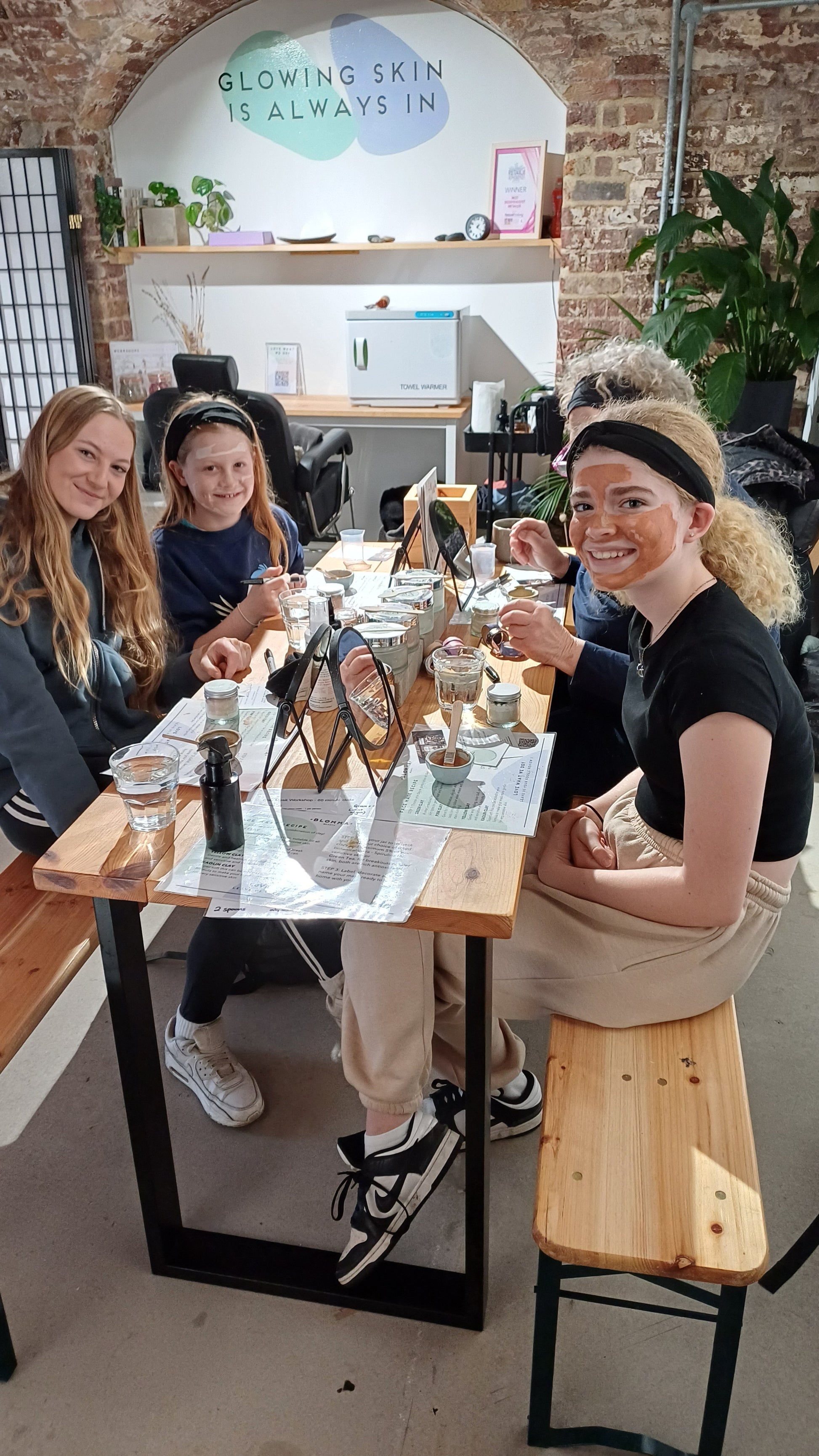 group of young girls and their grandmother at our make your own clay face mask class in london. sitting around a wooden table with their mask formulations waiting to apply it to their skin