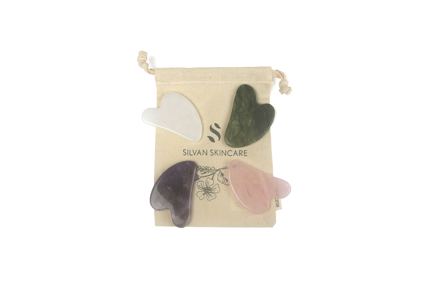 flat lay photo of white, green, pink and purple gua sha tools laid on top of a cream coloured organic cotton drawstring bag