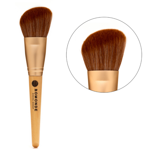photo of bomonde's large angled make up brush on a white background. on the left you can see the chestnut coloured bristles of the brush which are angled to add definition and contouring to your make up looks. there is a gold metal texture to help join the bristles to the yellow bamboo wooden handle which has the black bomonde logo printed on it. to the right of the image there is a close up of the cruelty free synthetic brush bristles in a circle