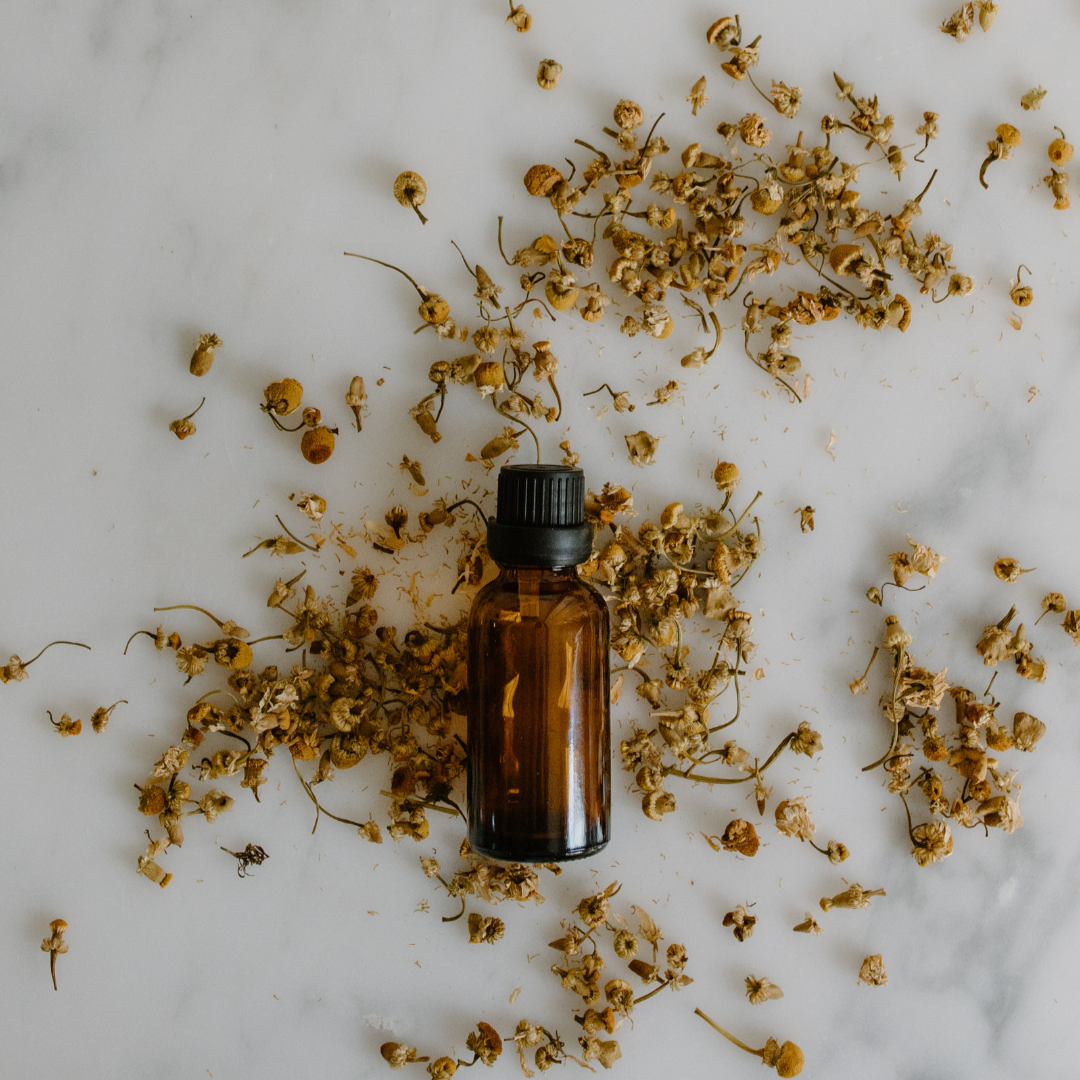 marble surface scattered with dried flowers and a brown lass bottle with black lid is visible. used to show an example face oil blend hand made as part of the make your own skincare workshop/event in london