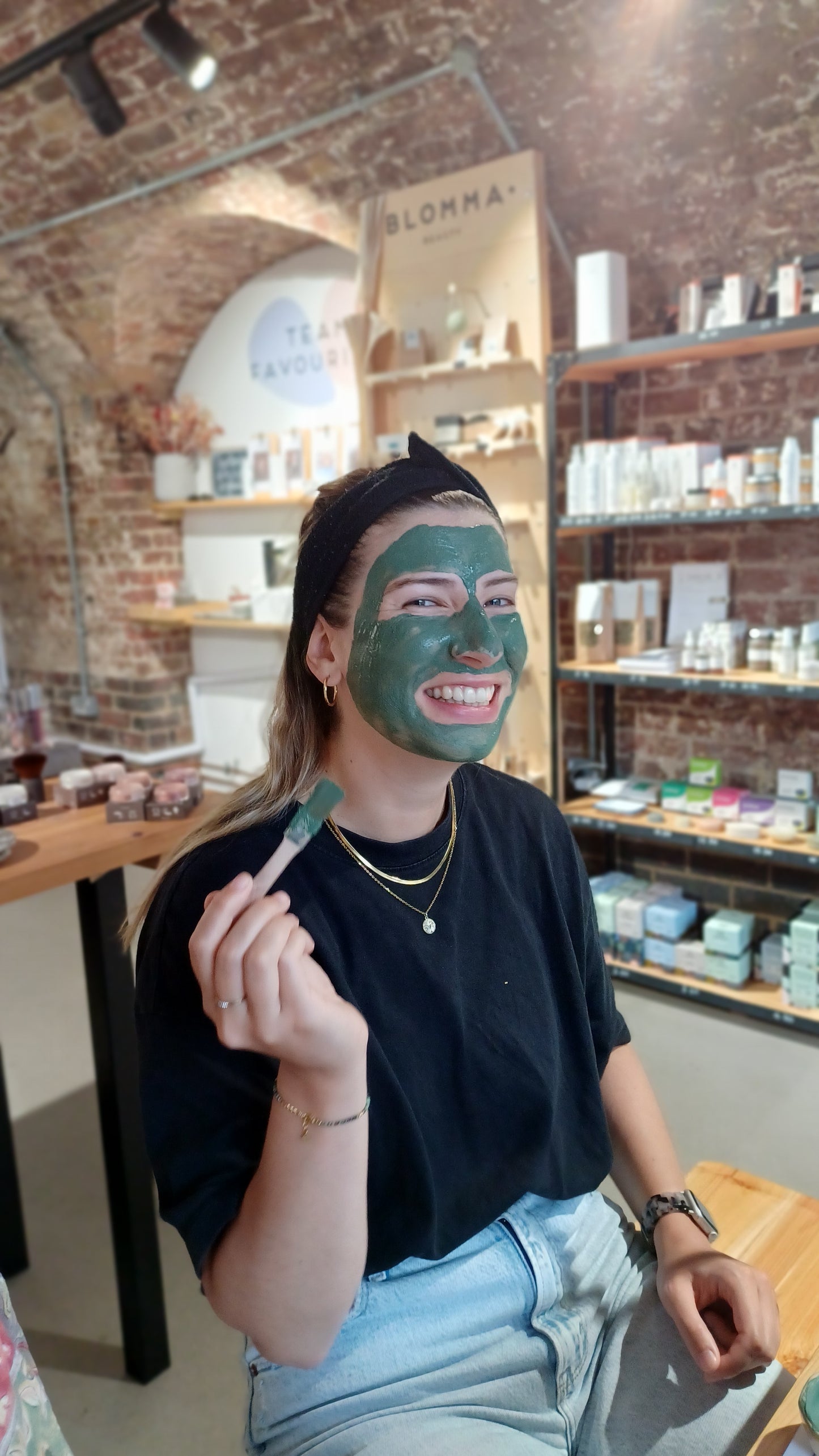 smiling woman with face mask brush in hand having just applied her custom made face mask to her skin