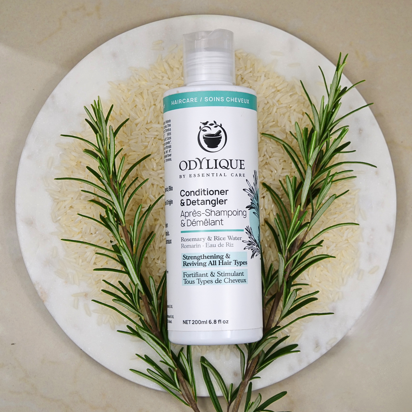 Odylique conditioner bottle with rosemary on a marble places with rice underneath it