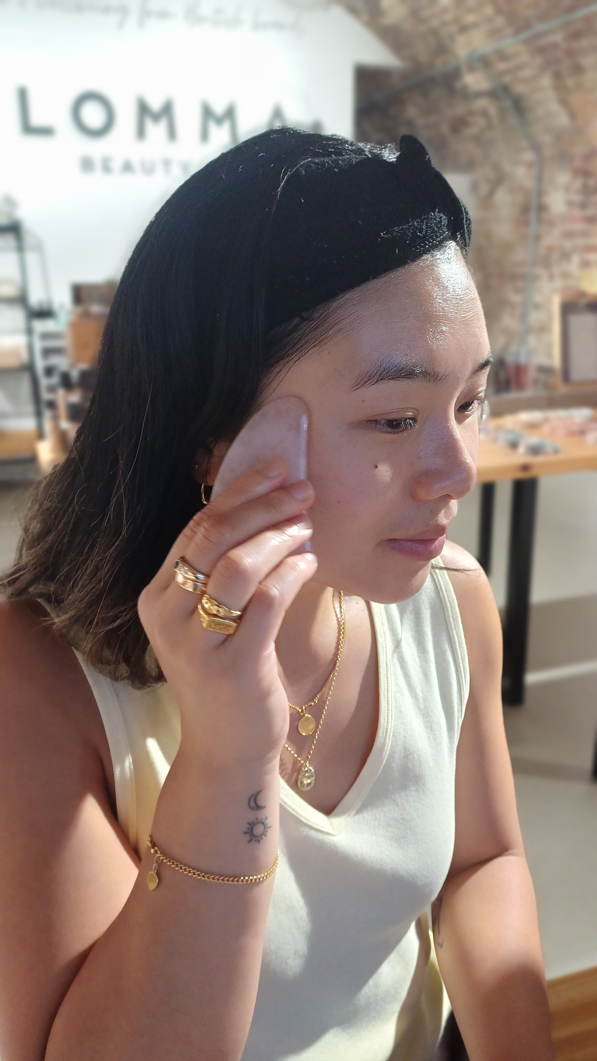 woman with dark hair wearing a hair band massaging her gua sha tool on her temple at a blomma beauty gua sha facial massage tool