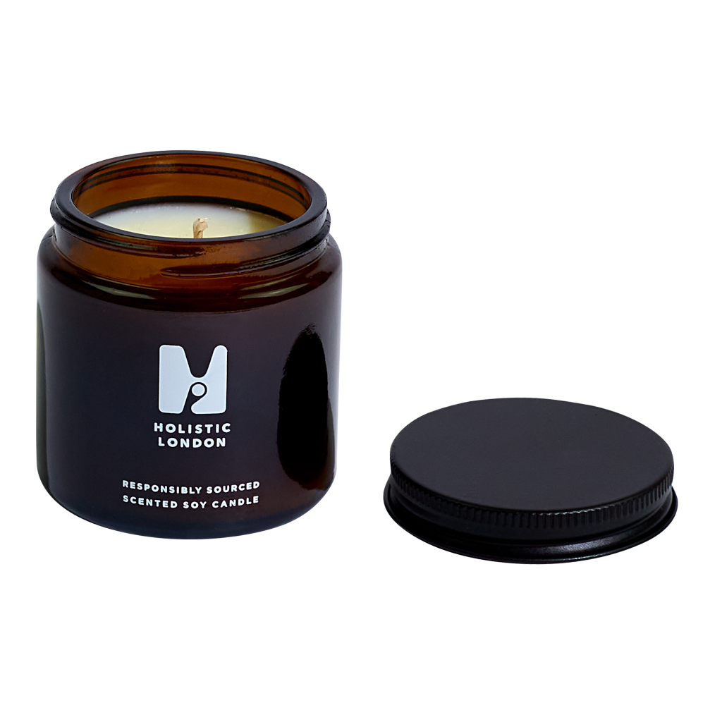 photograph of holistic london's bergamot + wildflowers 120g soy based candle on a white background. on the left side the photo is the amber jar which holds the candle and on the right side is the black aluminium lid laid next to it.