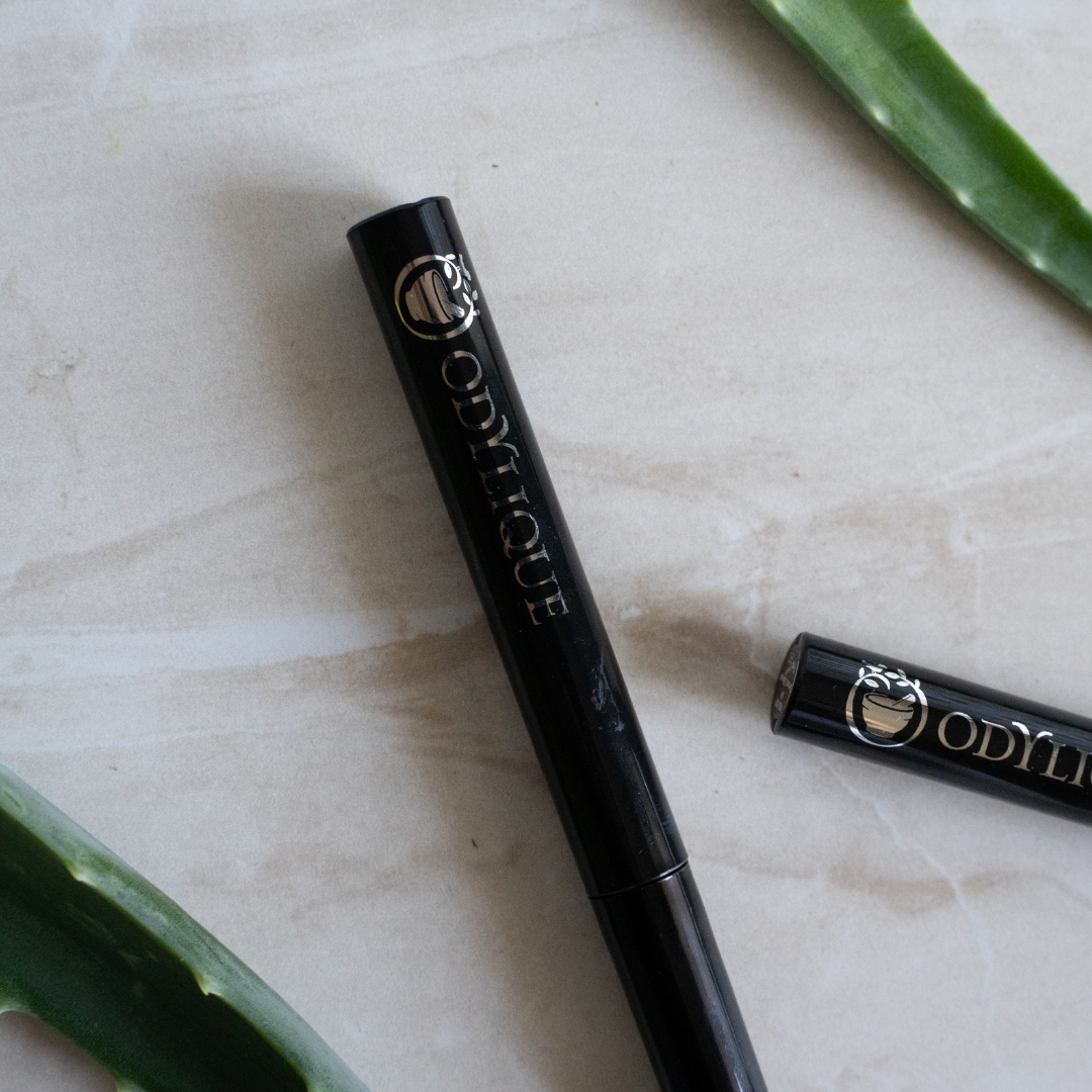 Odylique Mascara resting on a marble surface alongside aloe vera leaves.