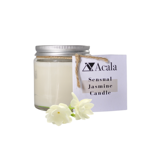 photo of acala zero waste's sensual jasmine candle on a white background. the candle comes in a clear glass jar with silver aluminium lid. there is some brown string which has a white card label attached to it which reads 'acala sensual jasmine candle'. in front of the candle are two buds of jasmine flowers
