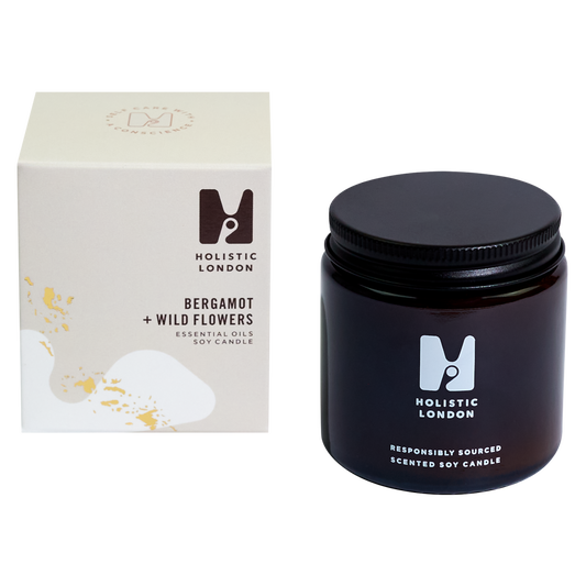 photograph of holistic london's bergamot + wildflowers 120g soy based candle on a white background. on the left side of the image is the light beige cardboard box with the holistic london logo on it. the label reads 'bergamot + wildflowers essential oils soy candle'. on the right side of the photo is the amber jar with a black aluminium lid which holds the candle. the glass is printed with the holistic london logo and says 'responsibly sourced scented soy candle'