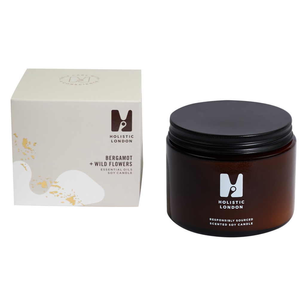 photograph of holistic london's bergamot + wildflowers 500g soy based candle on a white background. on the left side of the image is the light beige cardboard box with the holistic london logo on it. the label reads 'bergamot + wildflowers essential oils soy candle'. on the right side of the photo is the amber jar with a black aluminium lid which holds the candle. the glass is printed with the holistic london logo and says 'responsibly sourced scented soy candle'
