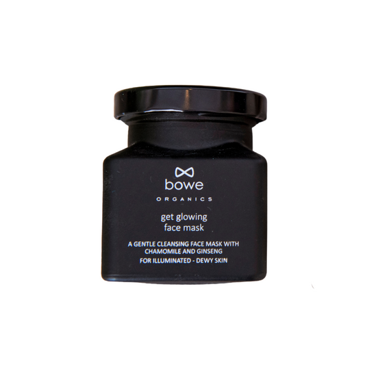 Bowe organics green clay powder face mask is photographed on a white background. the face mask comes in a coasted black glass jar and metal lid with white text that reads 'bowe organics get glowing face mask. a gentle cleansing face mask with chamomile and ginseng for illuminated, dewy skin'