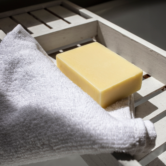 block of chamomile soap sitting on a wooden bath tray on top of a white fluffy cotton face towel