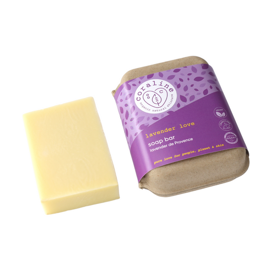 A bar of pale yellow soap next to its packaging. the wrapper is purple with ‘coraline lavender love soap bar’ written in white and details about lavender from provençe.