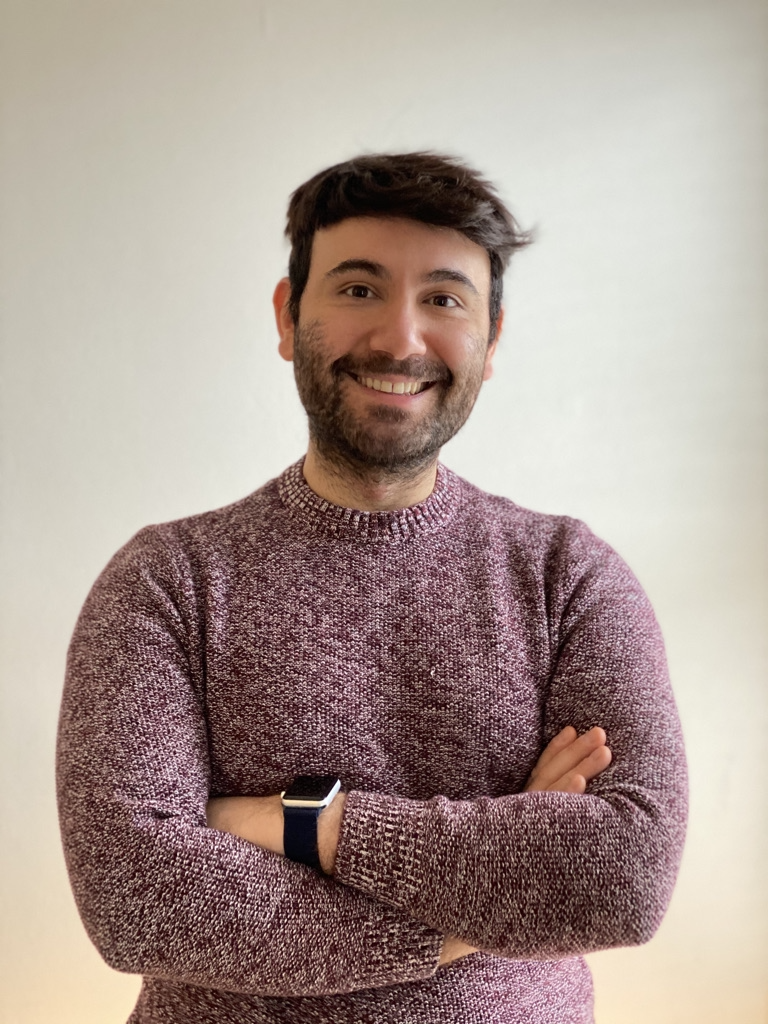 Haoma Founder Enis. He is shown smiling with his arms crossed wearing a burgundy and white cable knit sweater.