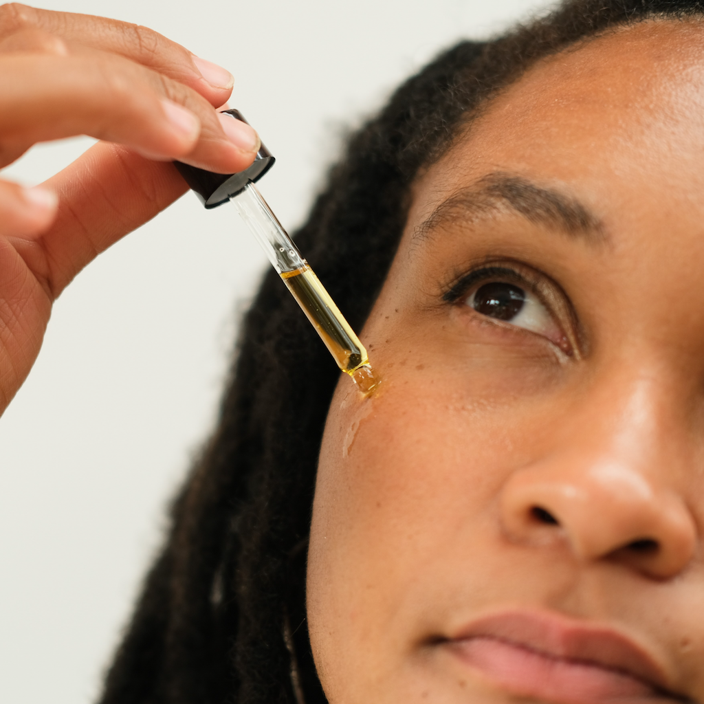 woman with brown skin and dark brown dreds applying inlight beauty's 100% organic face oil on to her cheek