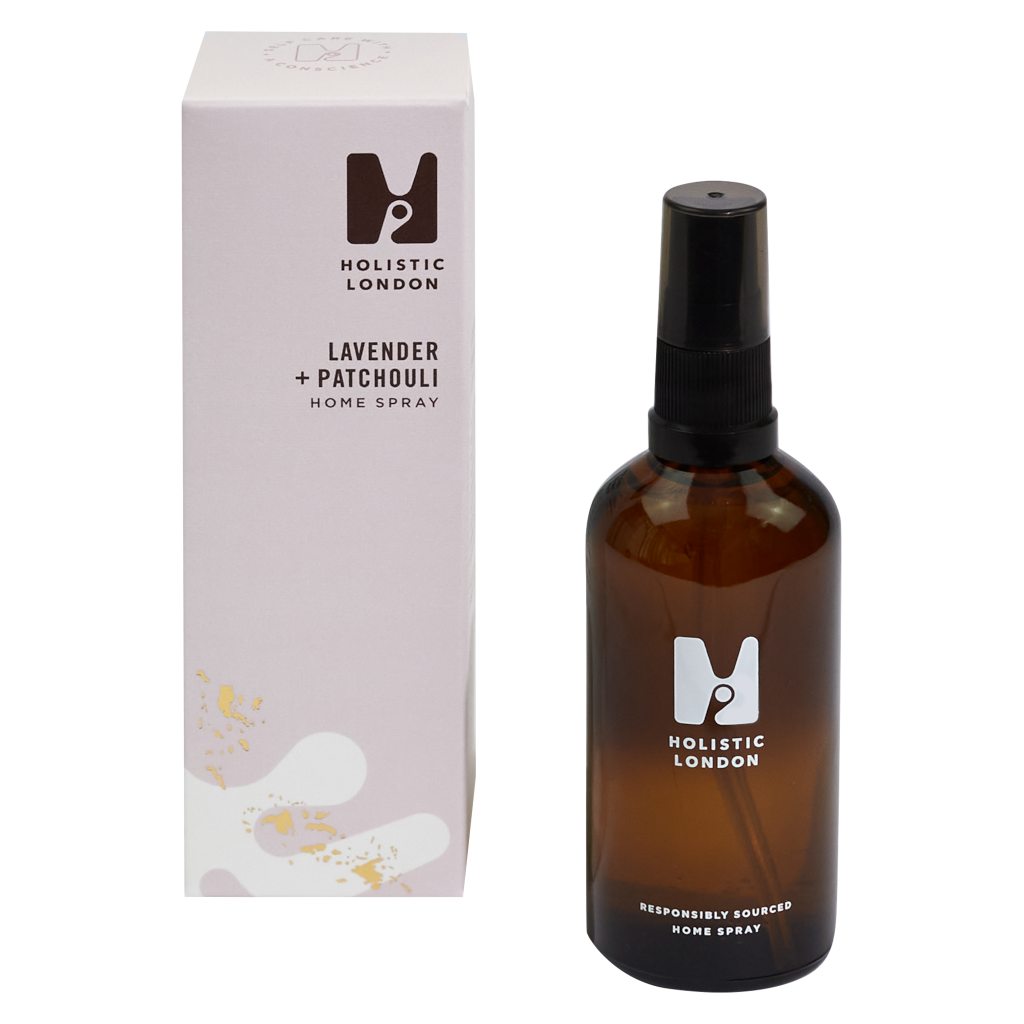 photograph of holistic london's lavender and patchouli home spray on a white background. on the left side of the image is the light purple cardboard box with the holistic london logo on it. the label reads ' lavender + patchouli homespray’. on the right side of the photo is the amber glass bottle with a black atomiser and lid which holds the spray. the glass is printed with the holistic london logo and says 'responsibly sourced home spray’