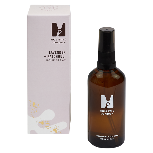 photograph of holistic london's lavender and patchouli home spray on a white background. on the left side of the image is the light purple cardboard box with the holistic london logo on it. the label reads ' lavender + patchouli homespray’. on the right side of the photo is the amber glass bottle with a black atomiser and lid which holds the spray. the glass is printed with the holistic london logo and says 'responsibly sourced home spray’
