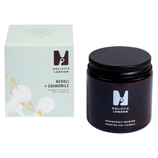 photograph of holistic london's neroli + chamomile 120g soy based candle on a white background. on the left side of the image is the light green cardboard box with the holistic london logo on it. the label reads 'neroli + chamomile essential oils soy candle'. on the right side of the photo is the amber jar with a black aluminium lid which holds the candle. the glass is printed with the holistic london logo and says 'responsibly sourced scented soy candle'